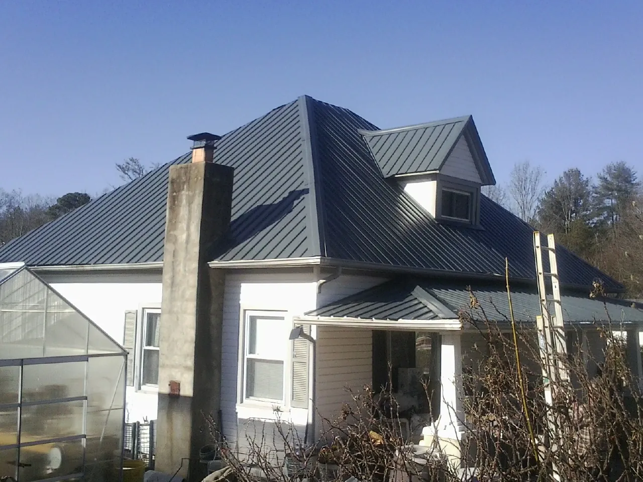 Dark blue standing seam metal roof on a white farmhouse with dormer — Slate & Tile Roof Repair by Roofing Brothers in Glade Valley
