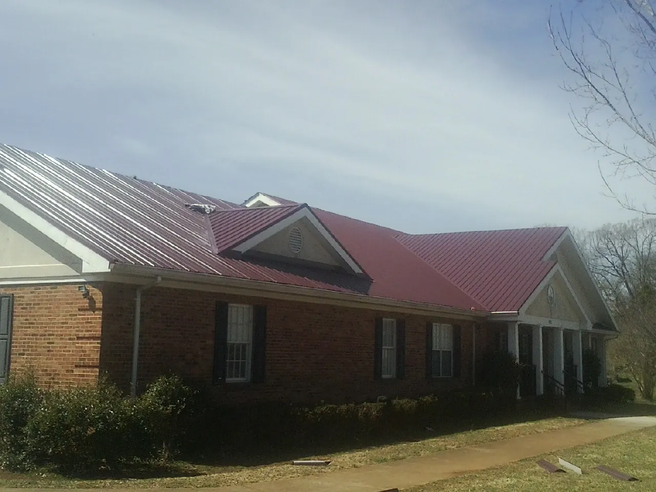 Red metal roof with gabled entries on a long brick building, from a Hail Damage Roof Repair job in Glade Valley