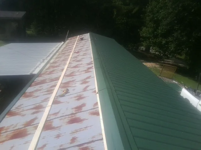 Old rusted panels beside newly installed green metal roofing — Wind Damage Roof Repair by Roofing Brothers in Glade Valley