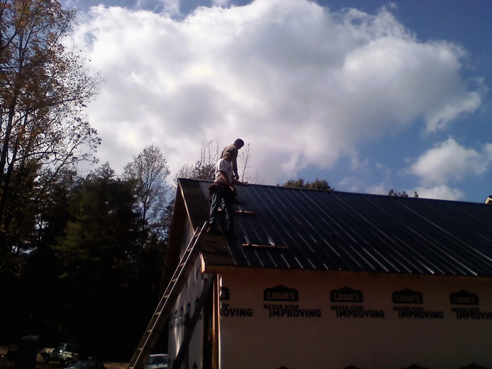 Roofer fastening dark metal panels high against a cloudy sky, from a Roof Inspection job in Glade Valley