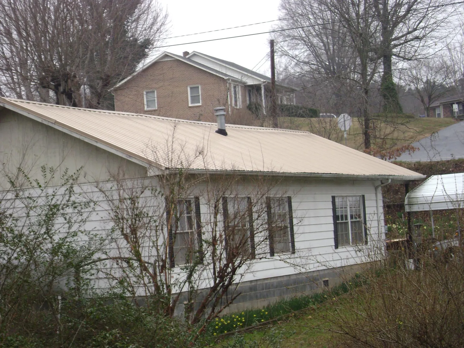 Tan metal roof on a white sided house set into a hillside — Commercial Roofing by Roofing Brothers in Glade Valley