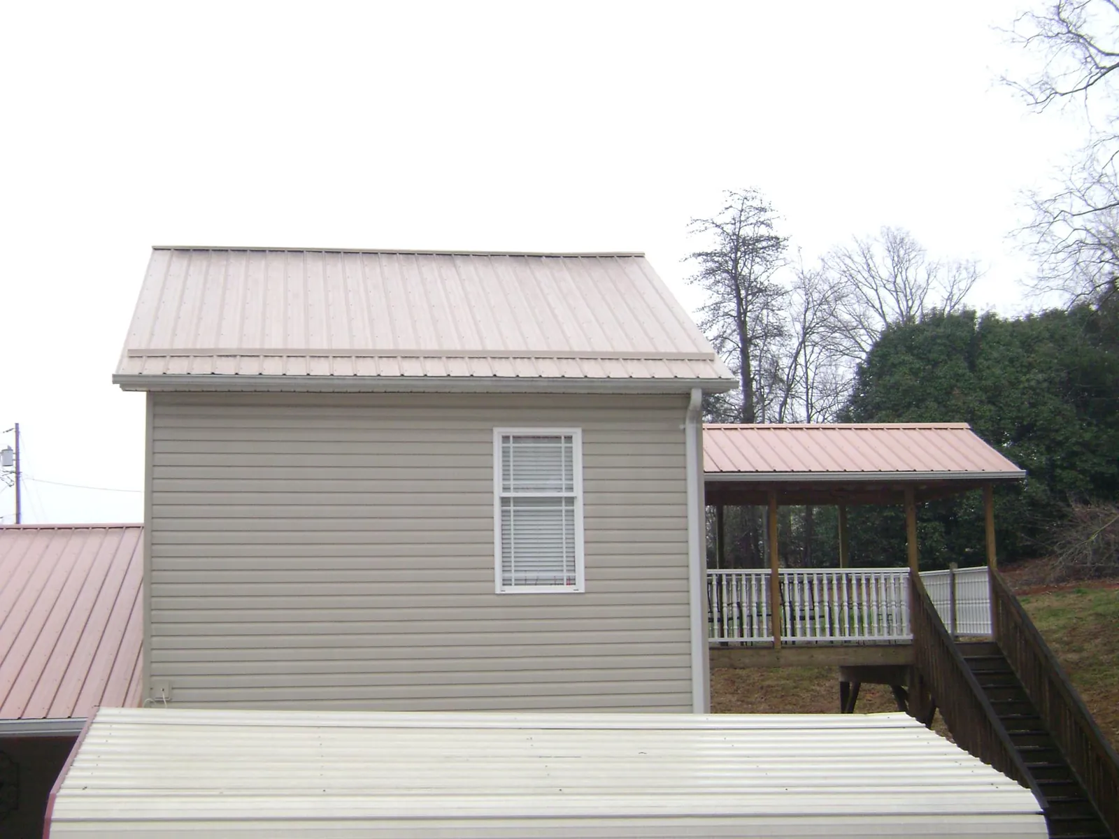 Tan metal roofs on a two story addition and attached porch, from a Roof Replacement job in Glade Valley